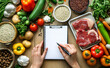 © Curioso.Photography - Hands write a grocery list on a notepad surrounded by fresh ingredients and raw meat.