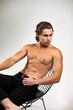 © Alex Vog - Stylish muscular man fashion model with perfect sexy bare torso sitting posing on chair, strong looking away. Sporty perfect guy with muscles abs press on white studio background. Copy ad text space