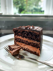 Poster - Layered chocolate cake on a plate with a kitchen window in the background