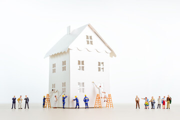 Miniature workers painting a white paper house with customers watching