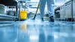 © Riko - Person cleaning commercial kitchen floor with mop. Low-angle view in industrial kitchen environment