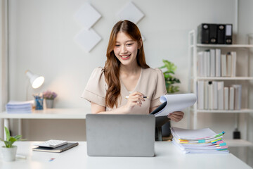 Wall Mural - A woman is sitting at a desk with a laptop and a stack of papers