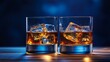 © klss777 - Two whisky glasses with ice glisten on a wooden table, illuminated by soft light against a blue backdrop.