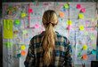 © 1by1step - A woman in casual attire, standing at an office whiteboard with colorful post-it notes and complex flow charts, focusing on creating creative designs for marketing materials, her back to the camera