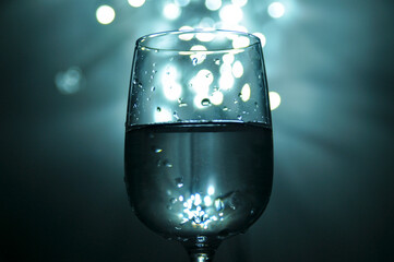 A glass filled with water, shades of blue, white bokeh from lights in the background