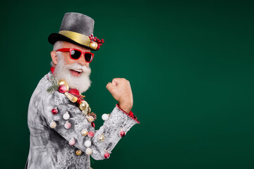 Poster - Profile portrait of delighted man christmas tree toys blazer cylinder hat raise fist empty space isolated on dark green color background