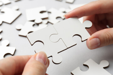 Wall Mural - Woman solving white puzzle on light grey background, closeup