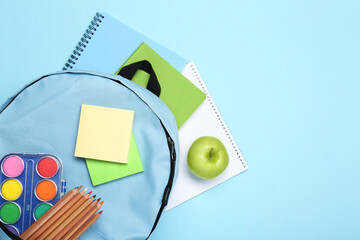 Wall Mural - Backpack with different school stationery on light blue background, flat lay. Space for text