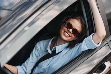 smiling woman with sunglasses sitting in car's driver seat, sunroof open, looking out window, enjoying sunny day