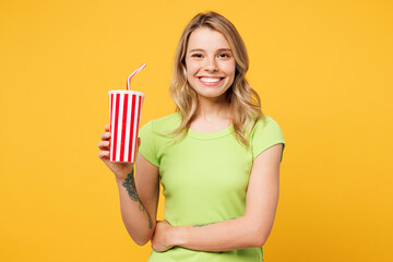 Wall Mural - Young happy blonde woman wear green t-shirt casual clothes hold in hand cup of soda pop cola fizzy water looking camera isolated on plain yellow orange background studio portrait. Lifestyle concept.