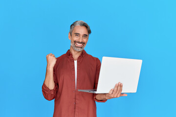 Happy middle aged business man entrepreneur, excited older professional businessman winner holding laptop celebrating online money profit, winning prize promotion standing isolated on blue background.