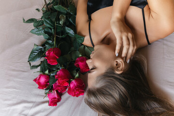 Canvas Print - A woman is laying on a bed with a bouquet of red roses next to her. Concept of romance and intimacy, as the woman is surrounded by the flowers and he is in a relaxed and comfortable position.