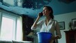 © nakarin - Woman Holding Bucket Under Leaky Roof While Talking on Phone in a Modern Home Interior
