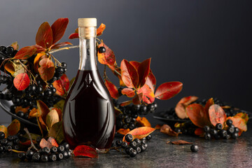 Black chokeberry juice and fresh berries on a black background.