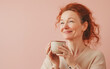 © nevolin andrii - A middle-aged woman with red hair, holding a mug and smiling contentedly while looking upward, radiating warmth and serenity against a soft pink background, suggesting a moment of peaceful reflection