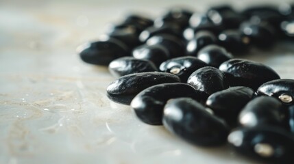 A bunch of black beans are spread out on a white surface