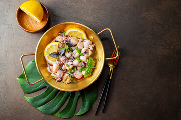 Mini cuttlefish fried with garlic, olive oil and lemon on dark background top view