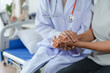 © amnaj - Doctor in white coat with stethoscope holding patient's hand in hospital room, offering comfort and compassion