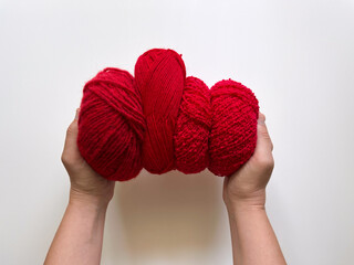 Top view of women's hands holding red woolen skeins for knitting. Supplies for knitting, crafts, and hobby.