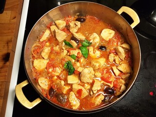 Pot on the stove with chicken stew with black olives, peppers, tomatoes, onion and basil.