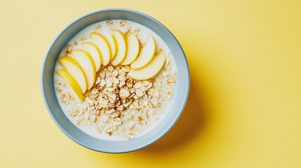 Wall Mural - A bowl of milk-based bircher muesli with apple slices, isolated on a soft pastel yellow background for a bright and healthy look