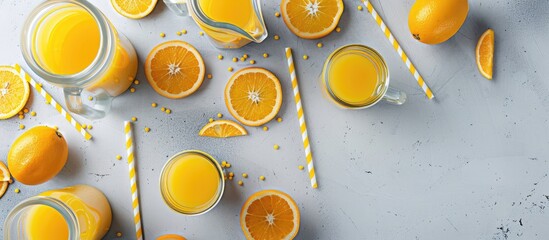 Canvas Print - Glass bottles cups and a pitcher filled with fresh orange juice accompanied by orange slices and yellow straws on a light gray table Top view Flat Lay. Copy space image