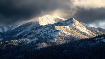 A rugged mountain ridge covered in fresh snow with sunlight breaking through dark clouds to illuminate the landscape.