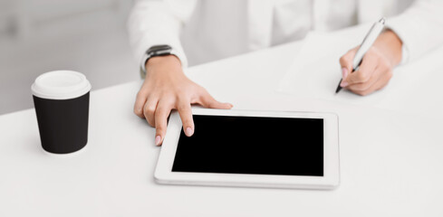 Poster - Close up view of young female writing her idea on notebook while touching her tablet in comfortable office room, mock up