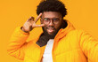 © Prostock-studio - Handsome winter afro guy making selfie over orange background, wearing glasses and showing peace symbol next to eye