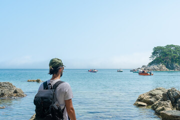 Wall Mural - a man looking out to sea with a backpack on his back.a man looking out to sea with a backpack on his back.