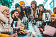 © Davide Angelini - Happy multiracial friends toasting red wine at restaurant terrace - Group of young people wearing winter clothes having fun at outdoors winebar table - Dining life style and friendship concept