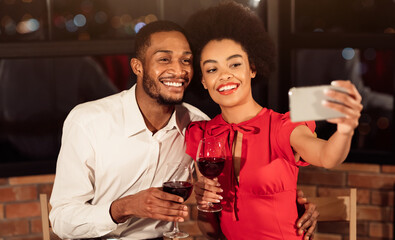 Valentine's Selfie. Happy African American Couple Making Self-Portrait On Smartphone Holding Wine Glasses Having Date In Restaurant