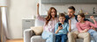 © Prostock-studio - A family of four joyfully reacts to a smartphone screen while gathered on a cozy couch in their living room. Their expressions show excitement and shared happiness.
