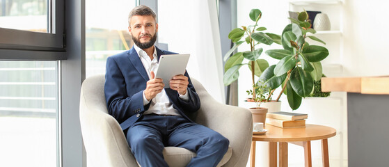 Wall Mural - Businessman with tablet computer sitting in armchair