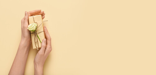 Female hands with gift box and beautiful white rose on yellow background. International Women's Day