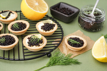 Grid of tasty tartlets with black caviar on green background