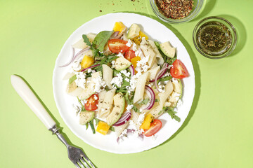 Plate of tasty pasta salad with tomatoes and avocado on green background