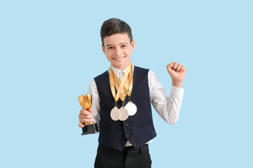 Canvas Print - Smart little school boy with prize cup and medals on light blue background