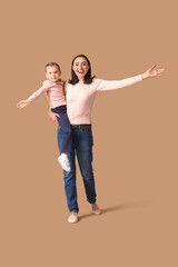 Wall Mural - Beautiful mother with her cute little daughter having fun together on brown background