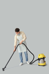 Wall Mural - Young man with vacuum cleaner on light background