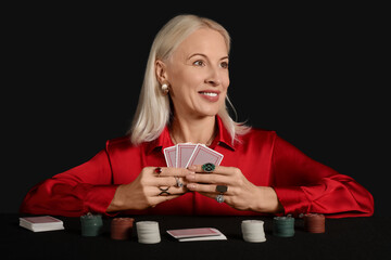 Canvas Print - Happy mature woman in beautiful earrings and rings playing poker at table on black background