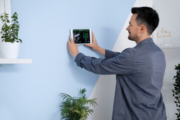 Canvas Print - Young man with smart home security system control panel in bedroom, back view