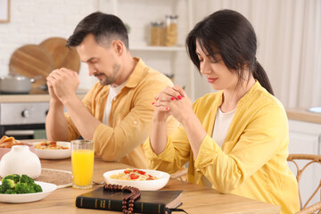 Canvas Print - Religious young woman with her husband praying before dinner at table in kitchen