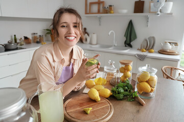 Canvas Print - Young woman with glass of lemonade at table in kitchen