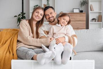 Little girl with her parents warming feet on radiator at home