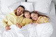 © Pixel-Shot - Happy parents with their little daughter lying under blanket on bed, top view