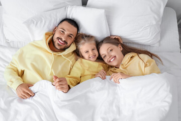 Poster - Happy parents with their little daughter lying under blanket on bed, top view