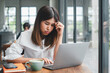 © Satori Studio - A young woman focused on her laptop while working in a modern cafe with large windows, natural light, and a cup of coffee.