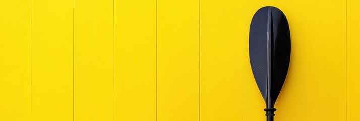 A black paddle against a vibrant yellow background, suggesting water sports or leisure activities.