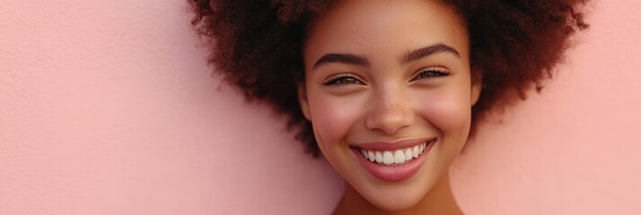 Wall Mural - A smiling individual with curly hair against a pink background, radiating joy and positivity.